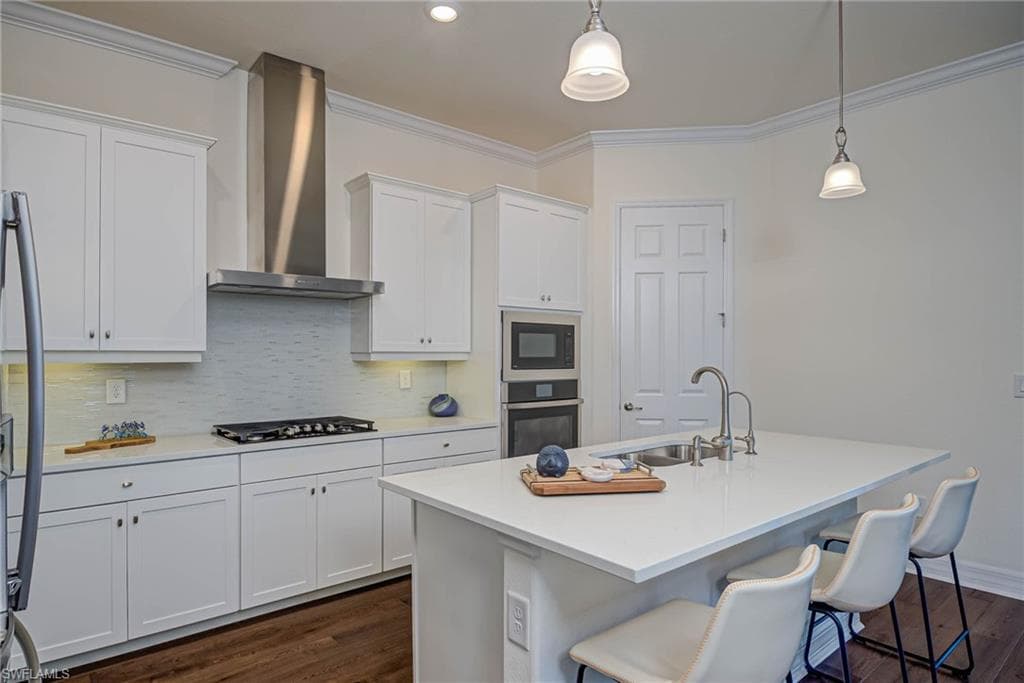 Kitchen with decorative backsplash, a breakfast bar area, dark wood-style flooring, white cabinetry, and ornamental molding