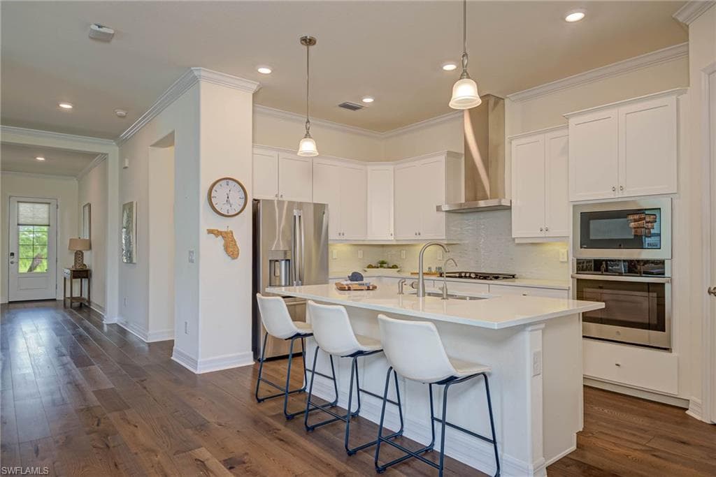 Kitchen featuring ornamental molding, backsplash, appliances with stainless steel finishes, white cabinets, and a center island with sink