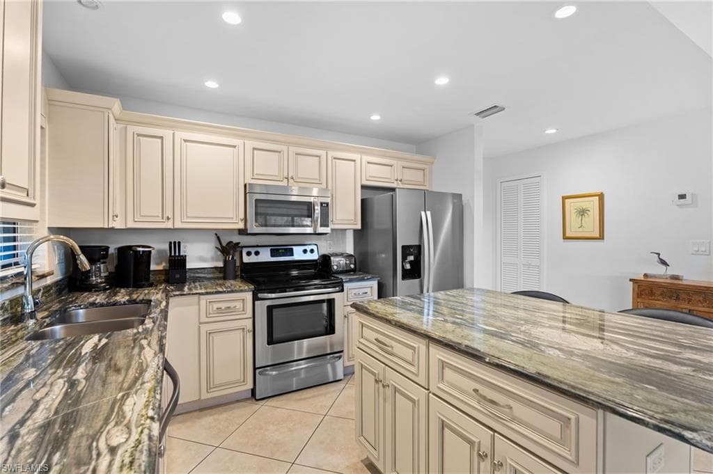 Kitchen featuring cream cabinets, dark stone countertops, appliances with stainless steel finishes, light tile patterned floors, and recessed lighting