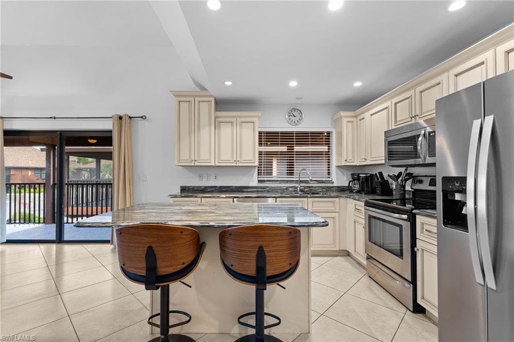 Kitchen featuring cream cabinets, dark stone counters, stainless steel appliances, a kitchen breakfast bar, and recessed lighting