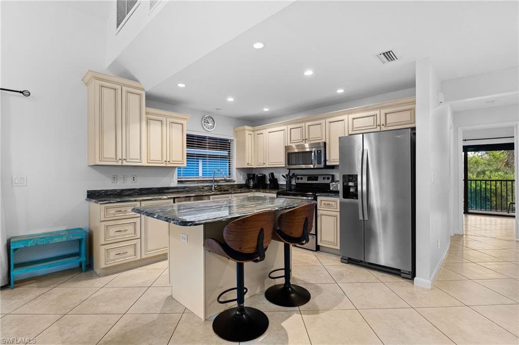 Kitchen featuring stainless steel appliances, dark stone countertops, a breakfast bar area, light tile patterned flooring, and recessed lighting
