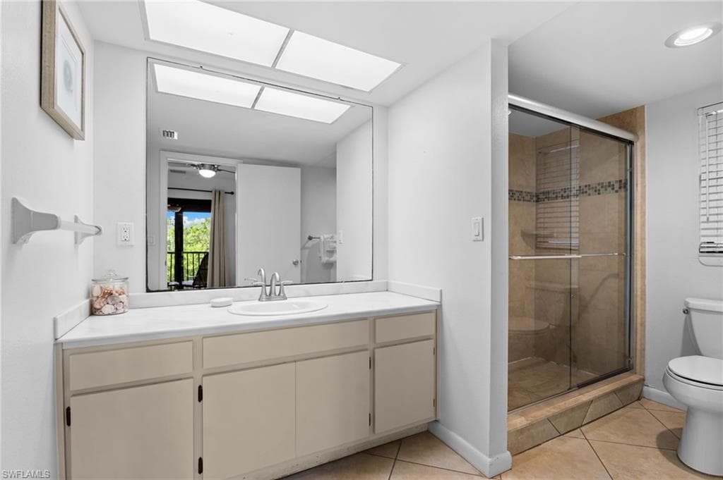 Full bathroom featuring light tile patterned floors, vanity, a shower stall, and a skylight