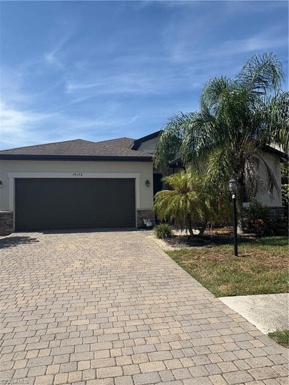View of front of property with stone siding, decorative driveway, stucco siding, and an attached garage
