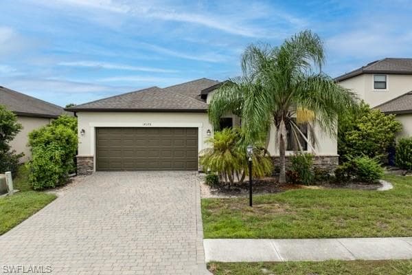 View of front of house featuring stucco siding, decorative driveway, stone siding, and a front yard
