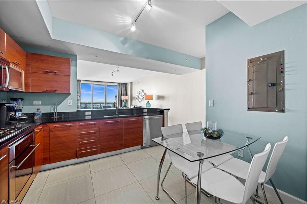 Kitchen featuring rail lighting, electric panel, appliances with stainless steel finishes, and dark stone countertops