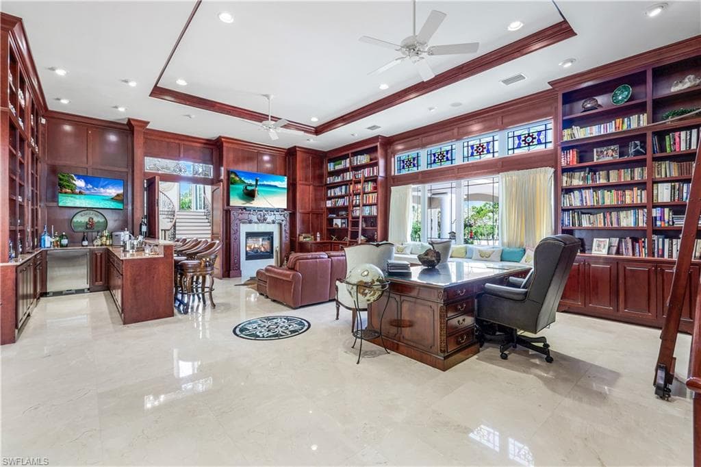 Office area with a tray ceiling, ceiling fan, a glass covered fireplace, crown molding, and recessed lighting