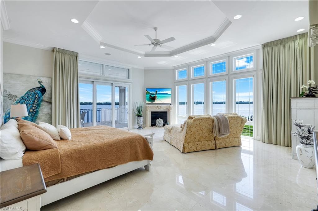 Bedroom with access to exterior, crown molding, a fireplace, a raised ceiling, and a high ceiling