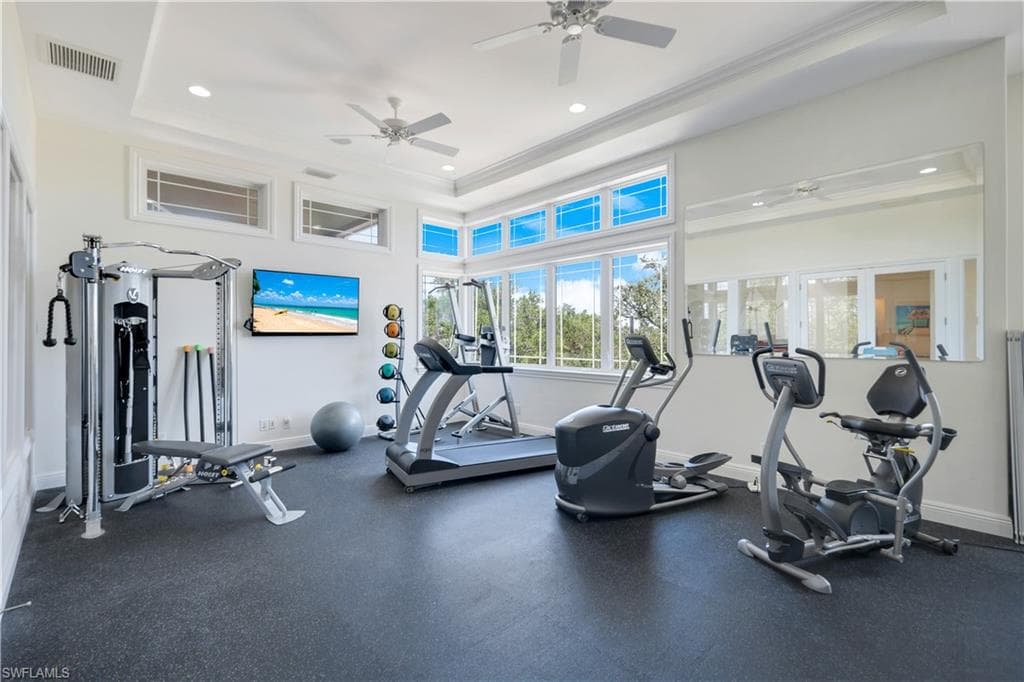 Workout area featuring a raised ceiling, ornamental molding, recessed lighting, and a ceiling fan