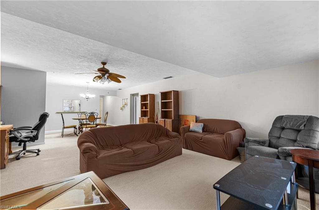 Living room with carpet flooring, a desk, ceiling fan, a textured ceiling, and a chandelier