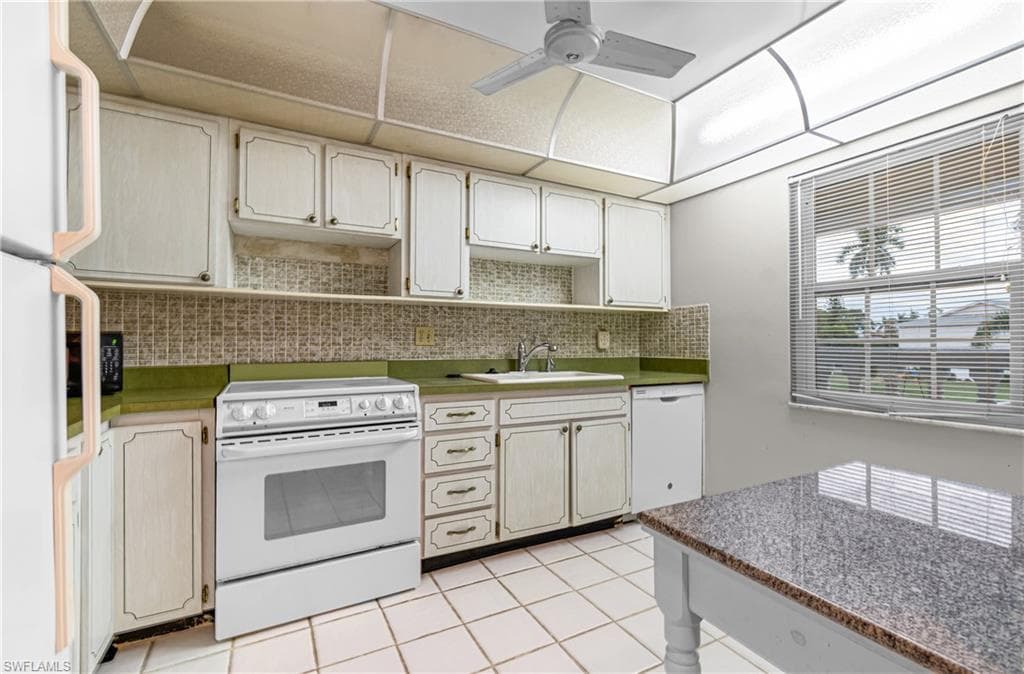 Kitchen featuring white appliances, backsplash, a ceiling fan, light tile patterned floors, and white cabinetry
