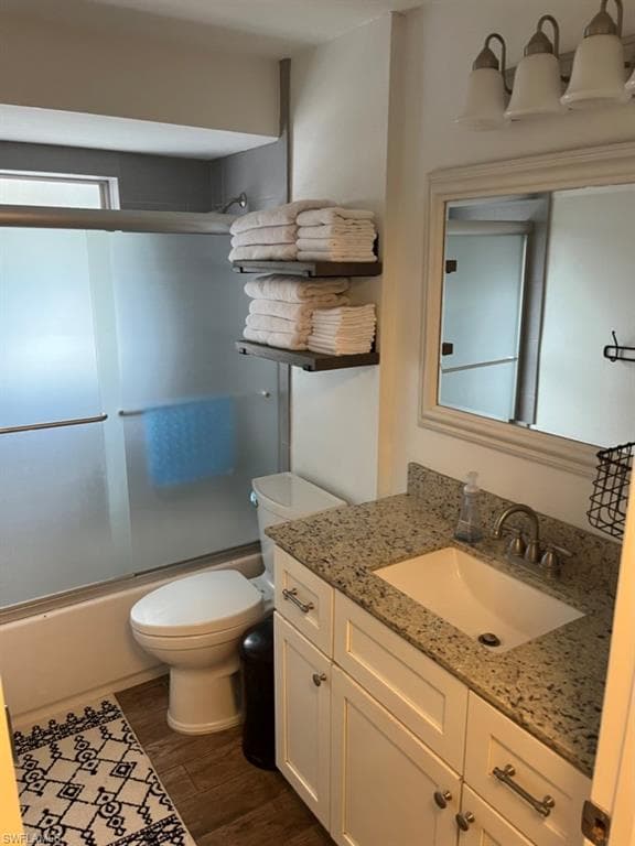 Full bath with combined bath / shower with glass door, vanity, and dark wood finished floors