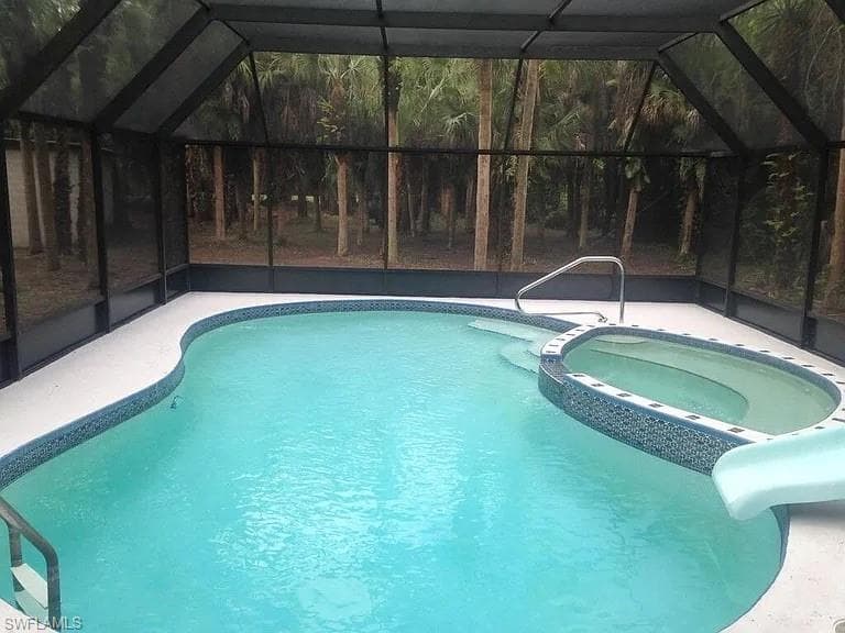 View of swimming pool with a sunroom, a water slide, a lanai, and a pool with connected hot tub