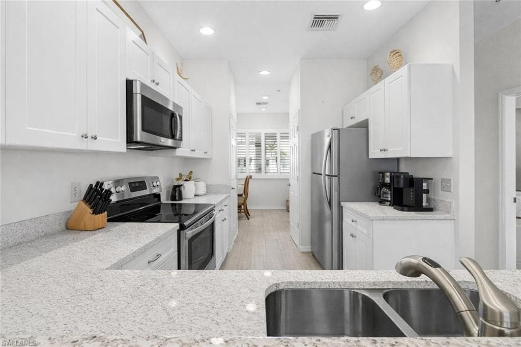 Virtual staged kitchen with stainless steel appliances, white cabinets, light stone counters, and recessed lighting