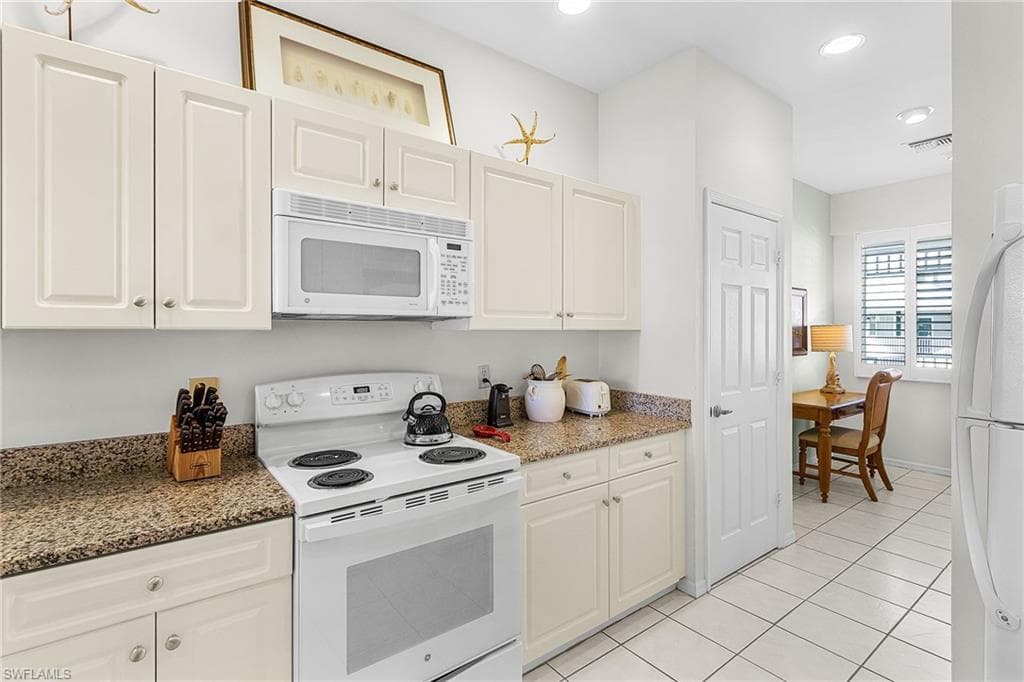 Kitchen with white appliances, dark stone countertops, light tile patterned floors, white cabinets, and recessed lighting