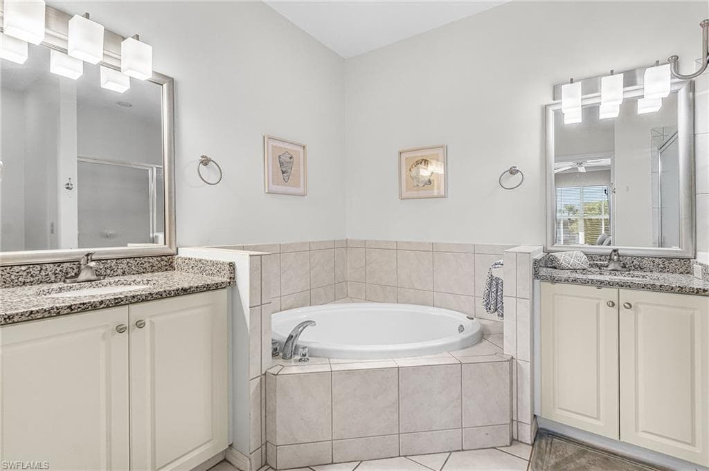 Full bathroom featuring a shower stall, a garden tub, two vanities, and light tile patterned flooring