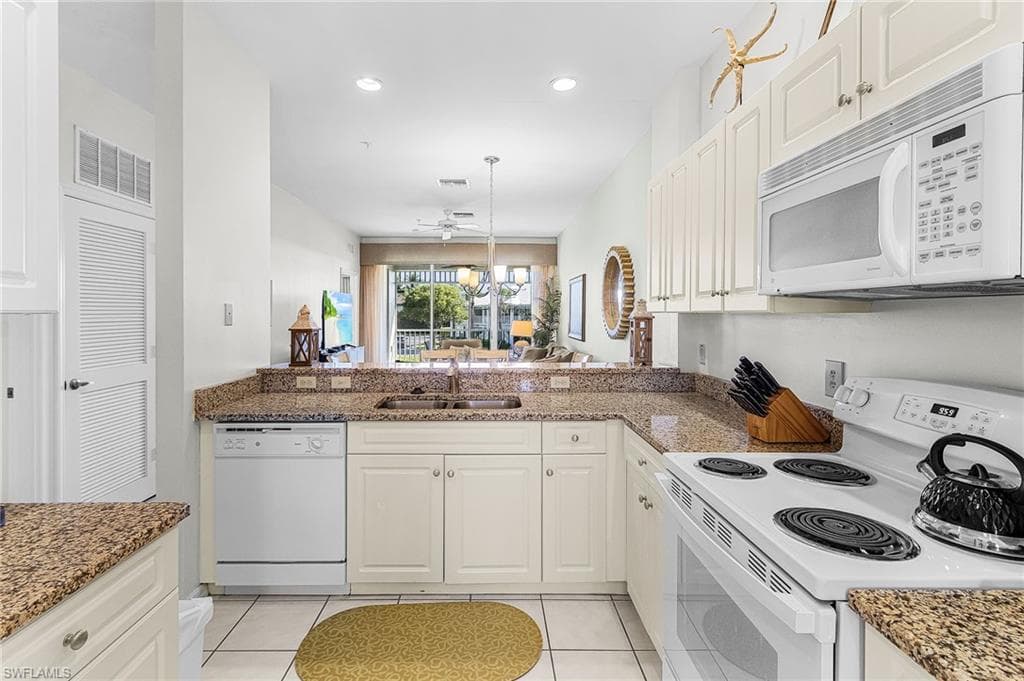 Kitchen with white appliances, white cabinets, light tile patterned flooring, light stone countertops, and recessed lighting