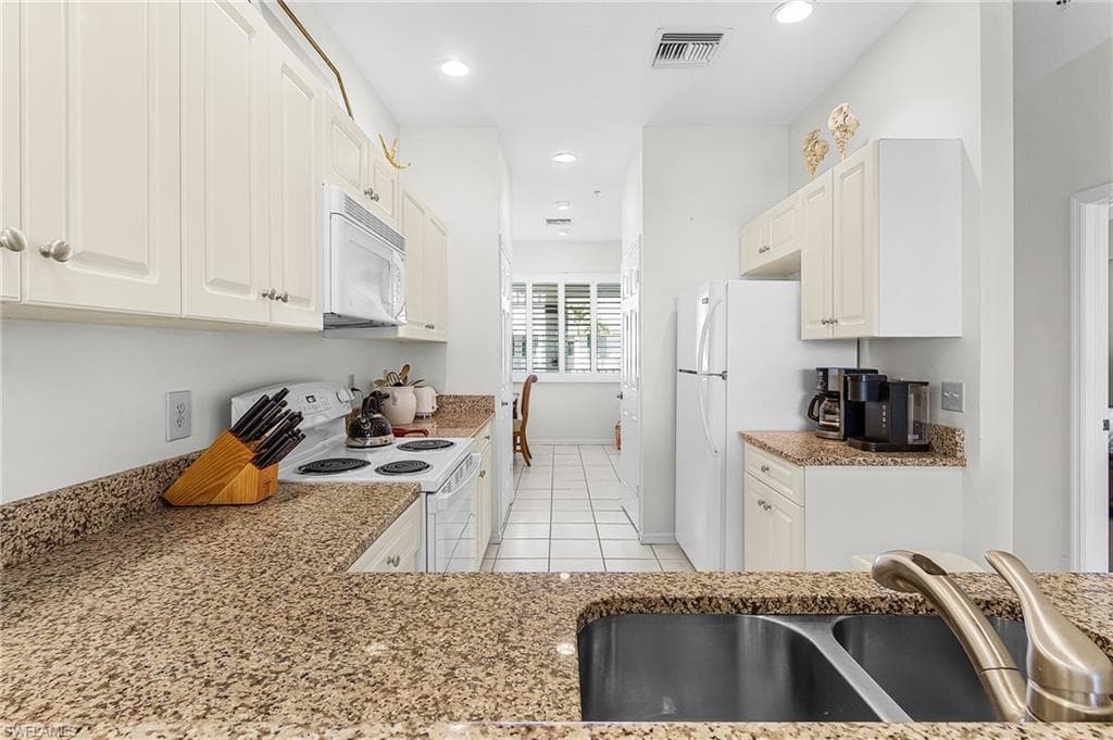 Kitchen with white appliances, white cabinets, recessed lighting, light tile patterned flooring, and light stone countertops