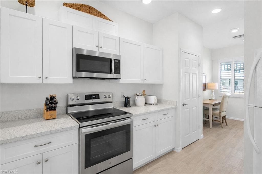Virtual staged kitchen with stainless steel appliances, white cabinets, light stone counters, and recessed lighting