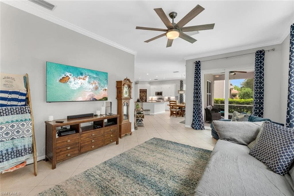 Living room with light tile patterned floors, ceiling fan, and crown molding