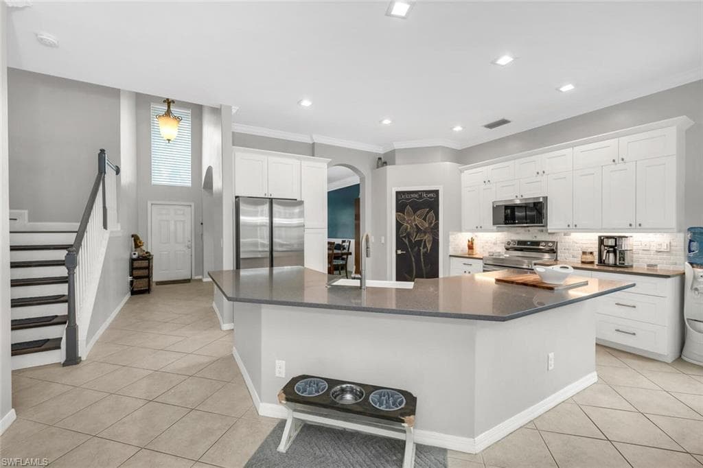 Kitchen featuring light tile patterned floors, tasteful backsplash, stainless steel appliances, white cabinets, and arched walkways