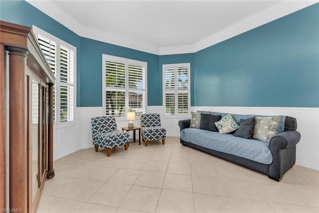 Sitting room with healthy amount of natural light, light tile patterned flooring, ornamental molding, and a wainscoted wall