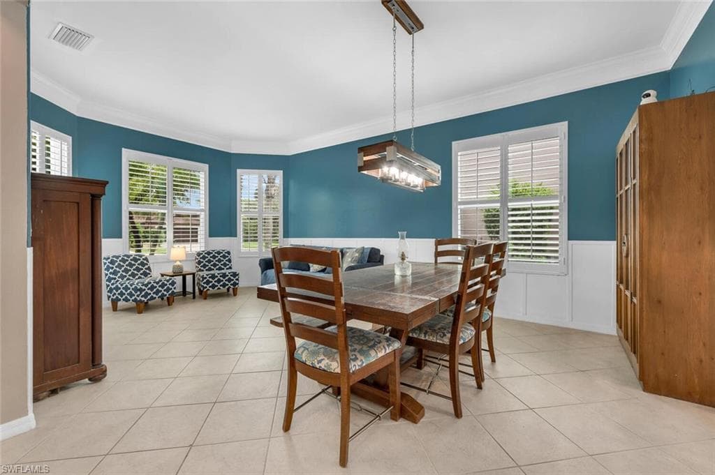 Dining space featuring ornamental molding, light tile patterned floors, and wainscoting