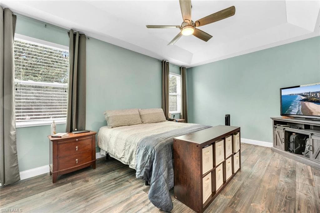 Bedroom featuring a raised ceiling, wood finished floors, and a ceiling fan