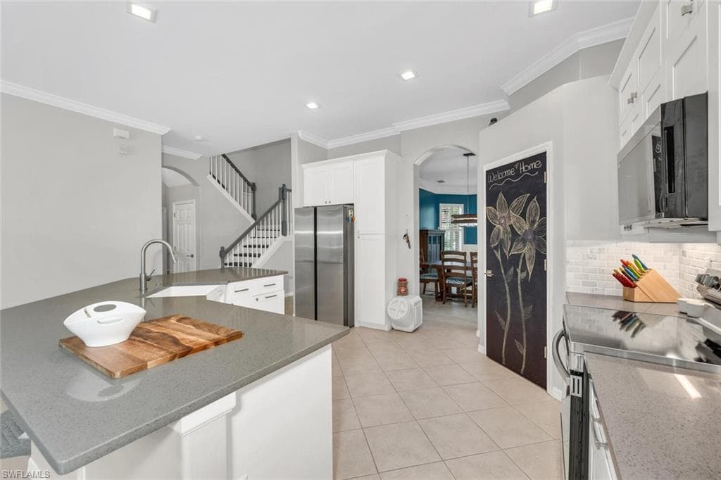 Kitchen featuring arched walkways, stainless steel appliances, dark stone counters, ornamental molding, and recessed lighting