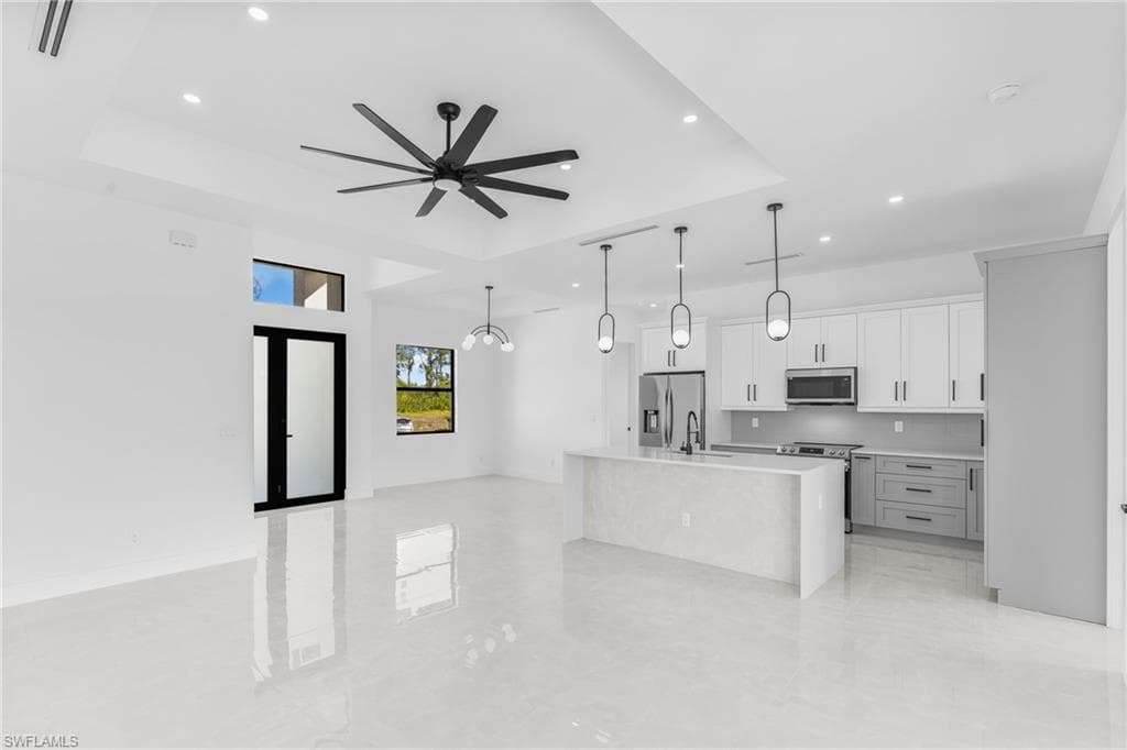 Kitchen with a tray ceiling, a center island with sink, white cabinetry, open floor plan, and hanging light fixtures