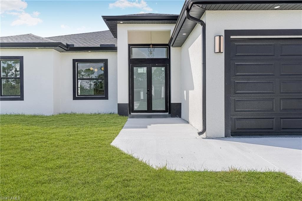View of exterior entry featuring stucco siding, a yard, an attached garage, and french doors
