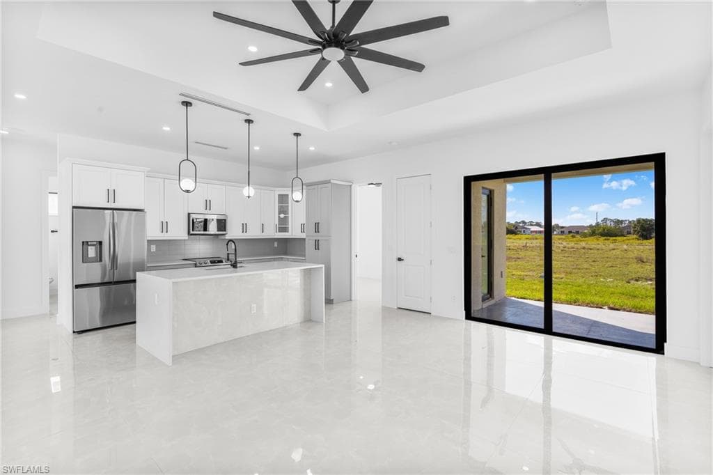 Kitchen with appliances with stainless steel finishes, a tray ceiling, glass insert cabinets, white cabinets, and an island with sink