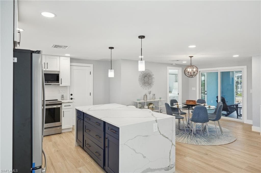 Kitchen featuring recessed lighting, stainless steel appliances, white cabinets, decorative light fixtures, and light stone countertops