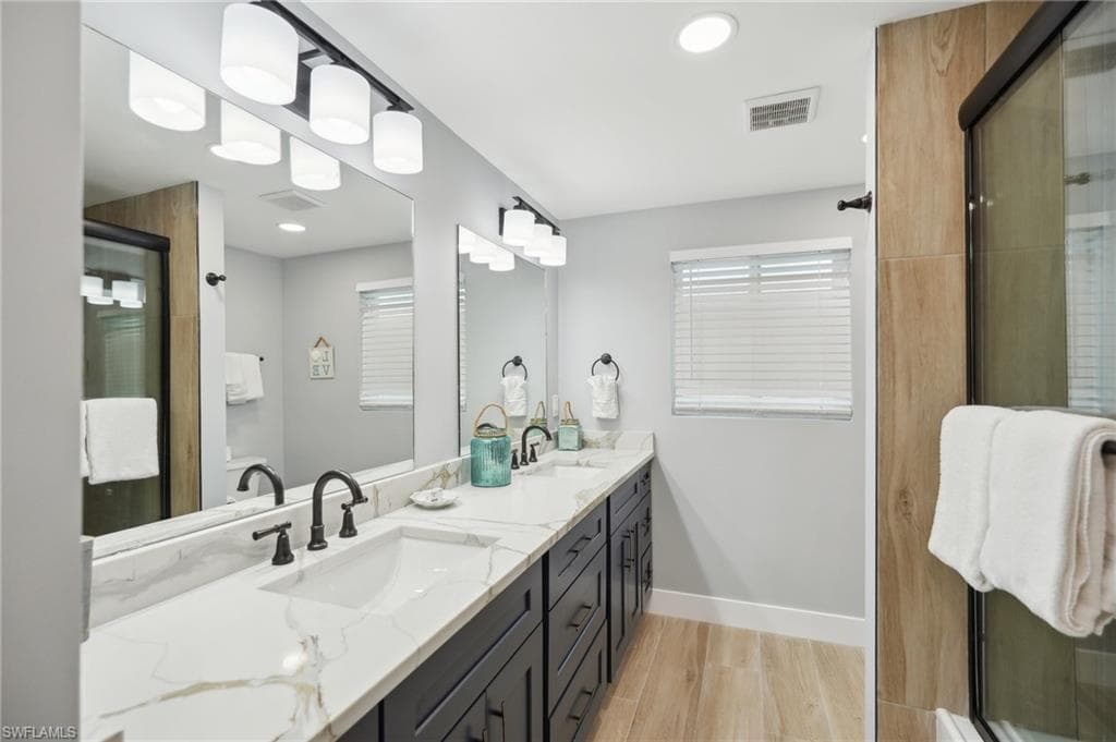 Full bath featuring light wood-type flooring, double vanity, recessed lighting, and a shower stall