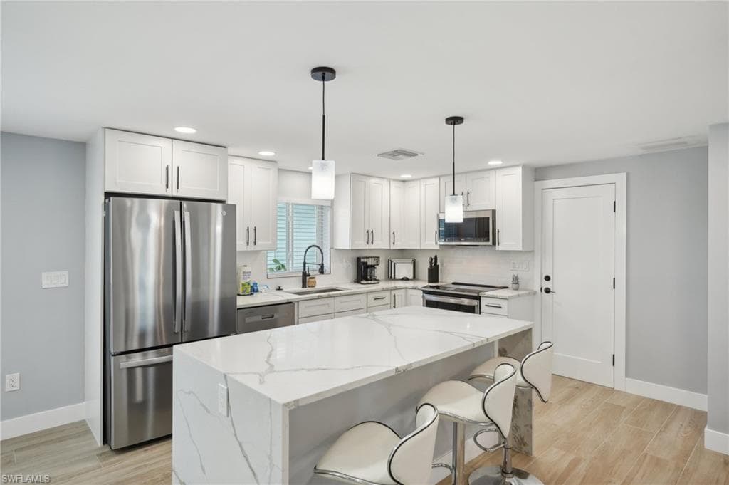 Kitchen with appliances with stainless steel finishes, white cabinetry, light stone counters, decorative light fixtures, and recessed lighting