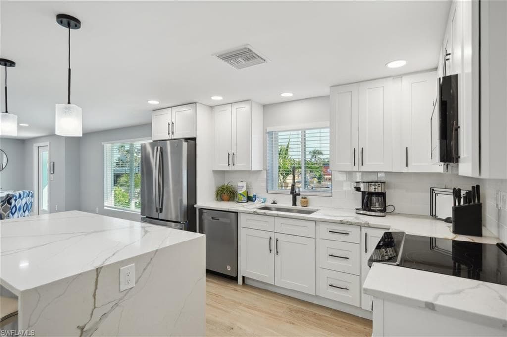 Kitchen with appliances with stainless steel finishes, light stone counters, light wood-type flooring, white cabinetry, and hanging light fixtures