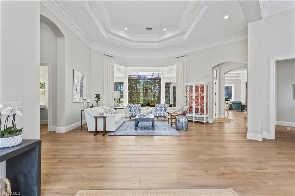 Living area with arched walkways, a towering ceiling, a tray ceiling, light wood-type flooring, and recessed lighting