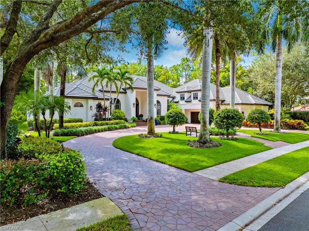 View of front facade with a front lawn, stucco siding, curved driveway, and a tiled roof