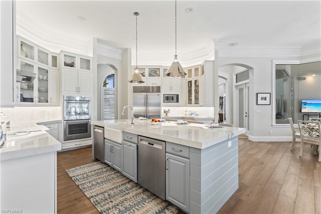 Kitchen with gray cabinetry, arched walkways, ornamental molding, glass insert cabinets, and built in appliances