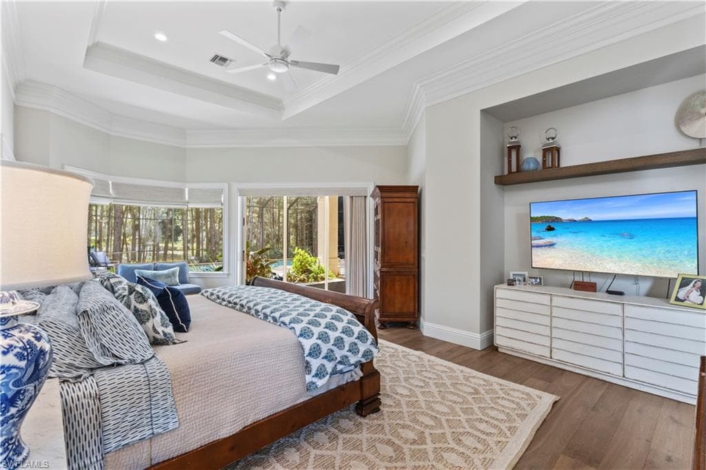 Bedroom featuring wood finished floors, a ceiling fan, a tray ceiling, ornamental molding, and recessed lighting