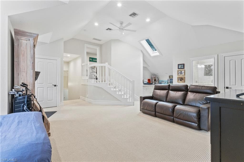 Living area featuring a skylight, carpet flooring, ceiling fan, high vaulted ceiling, and stairway