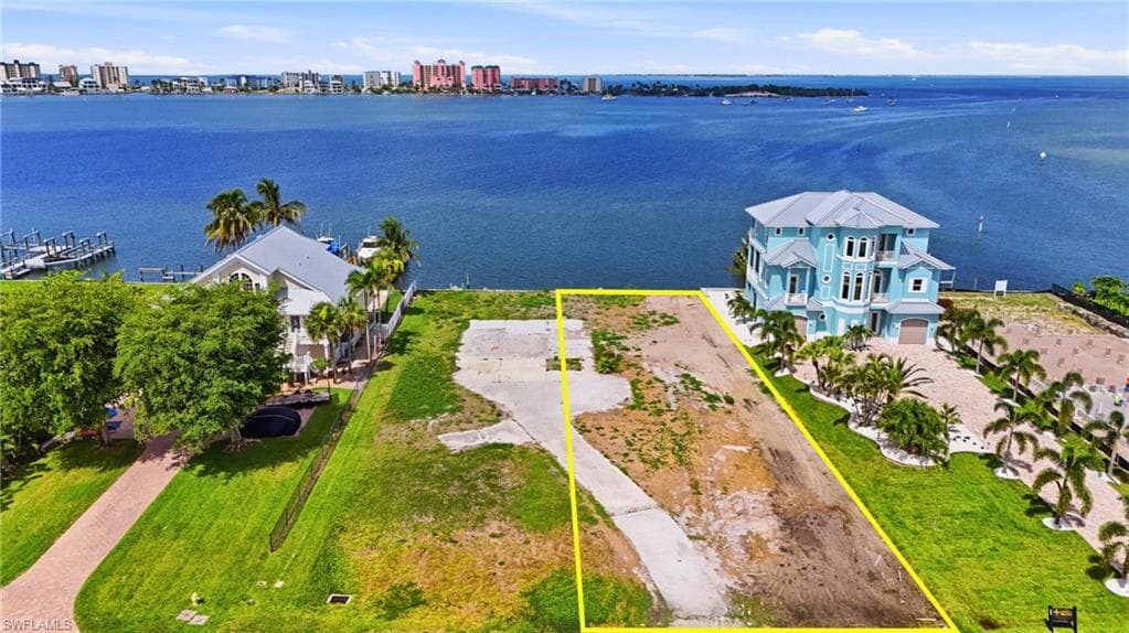 Waterfront lot with established concrete driveway, bordered by green landscaping and mature palm trees- Virtually Edited Image