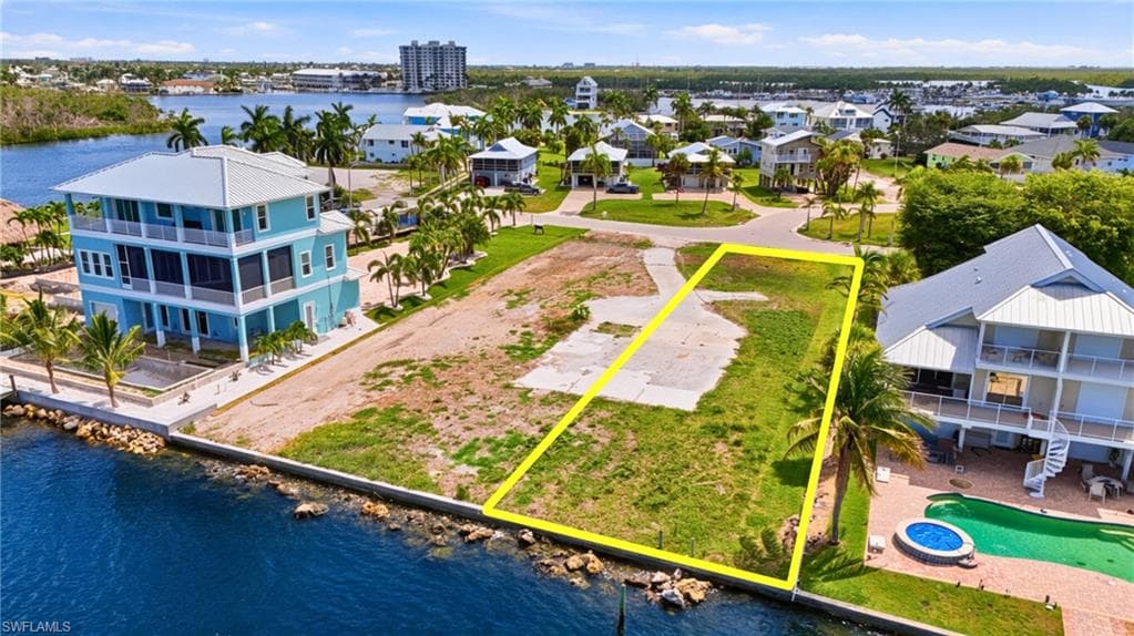 Waterfront lot featuring a concrete seawall, existing concrete driveway, and mature palm trees - Virtually Edited Image