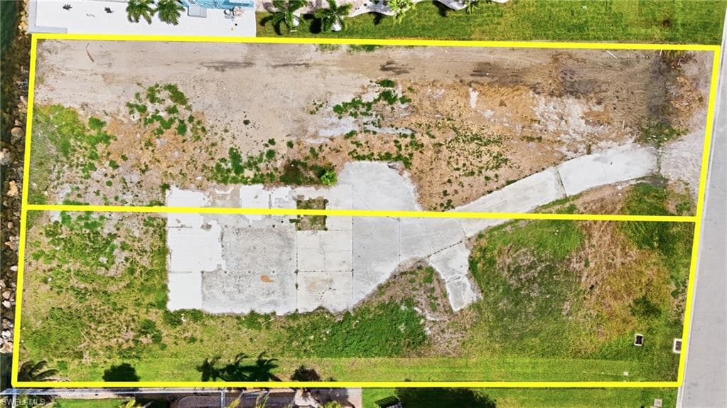 Expansive aerial view of a vacant lot with a concrete driveway and existing concrete pads - Virtually Edited Image