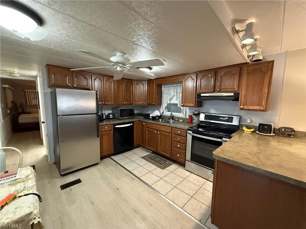 Kitchen with stainless steel appliances, brown cabinets, light wood-style floors, under cabinet range hood, and a textured ceiling