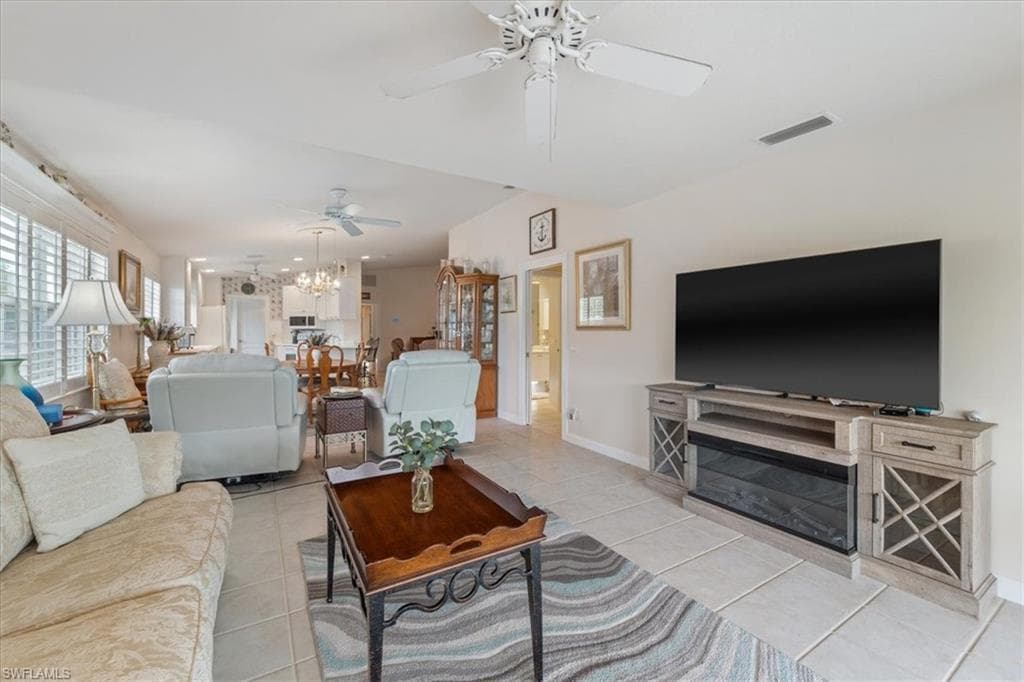 Living area with light tile patterned floors, a ceiling fan, and a glass covered fireplace