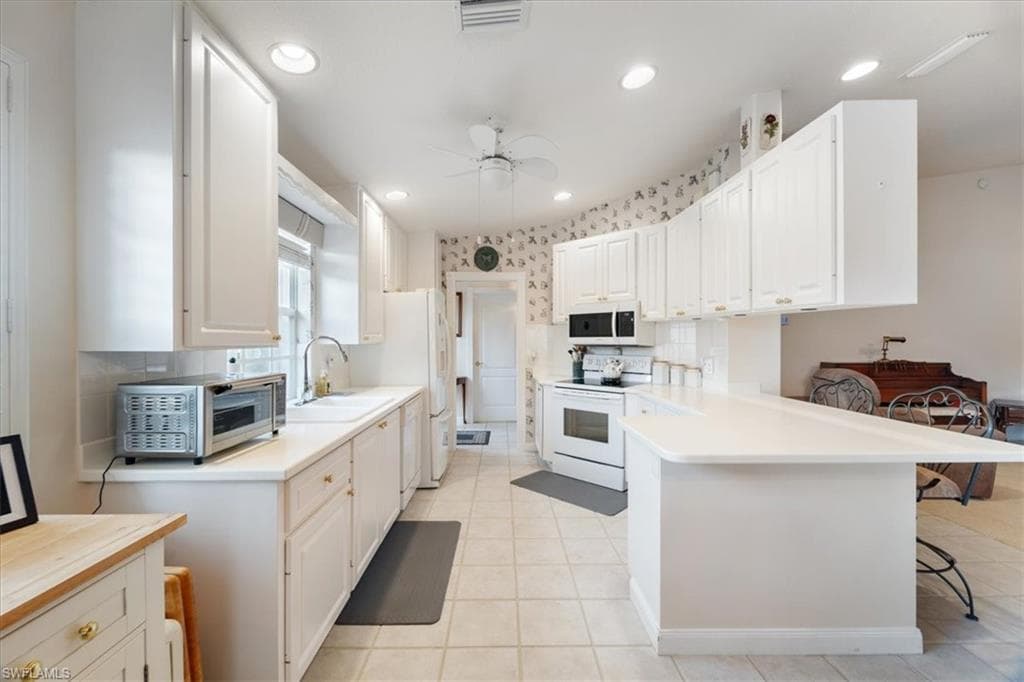 Kitchen with light countertops, white appliances, a kitchen bar, white cabinetry, and light tile patterned floors