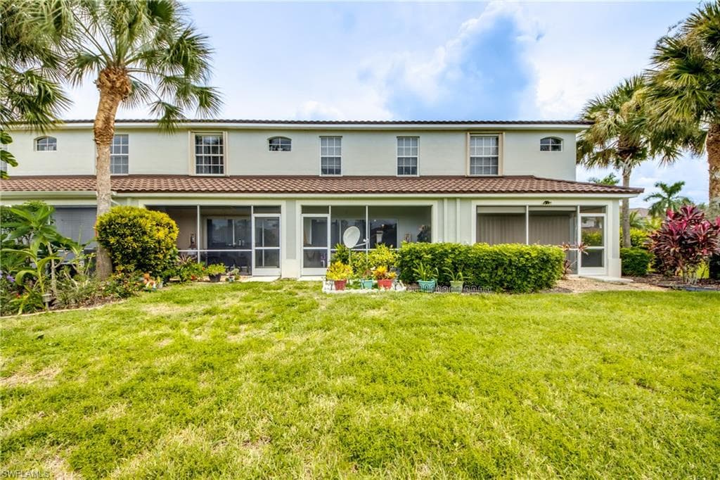 Back of property with a sunroom, stucco siding, a lawn, and a tiled roof