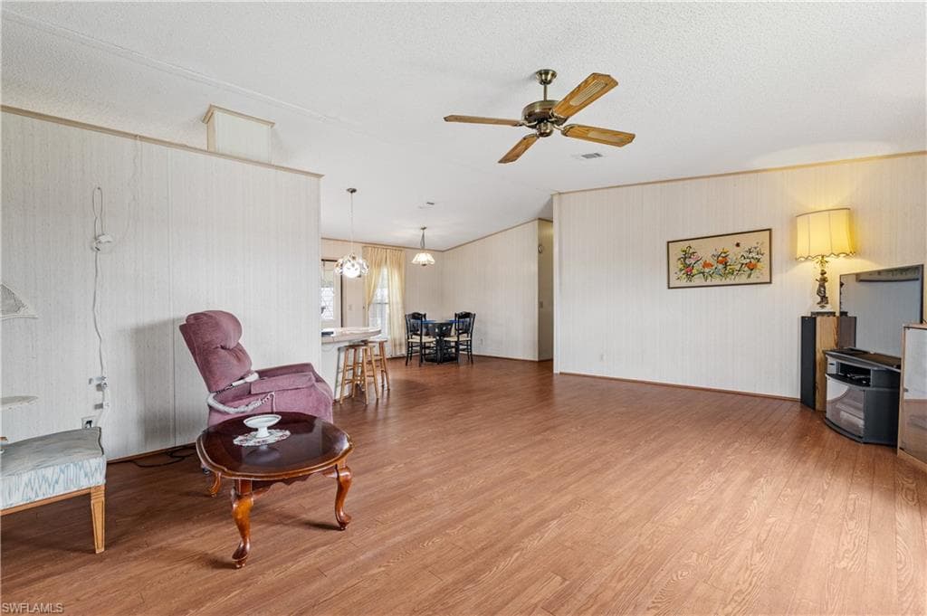 Living area featuring light wood-style flooring, ceiling fan, a textured ceiling, and a chandelier