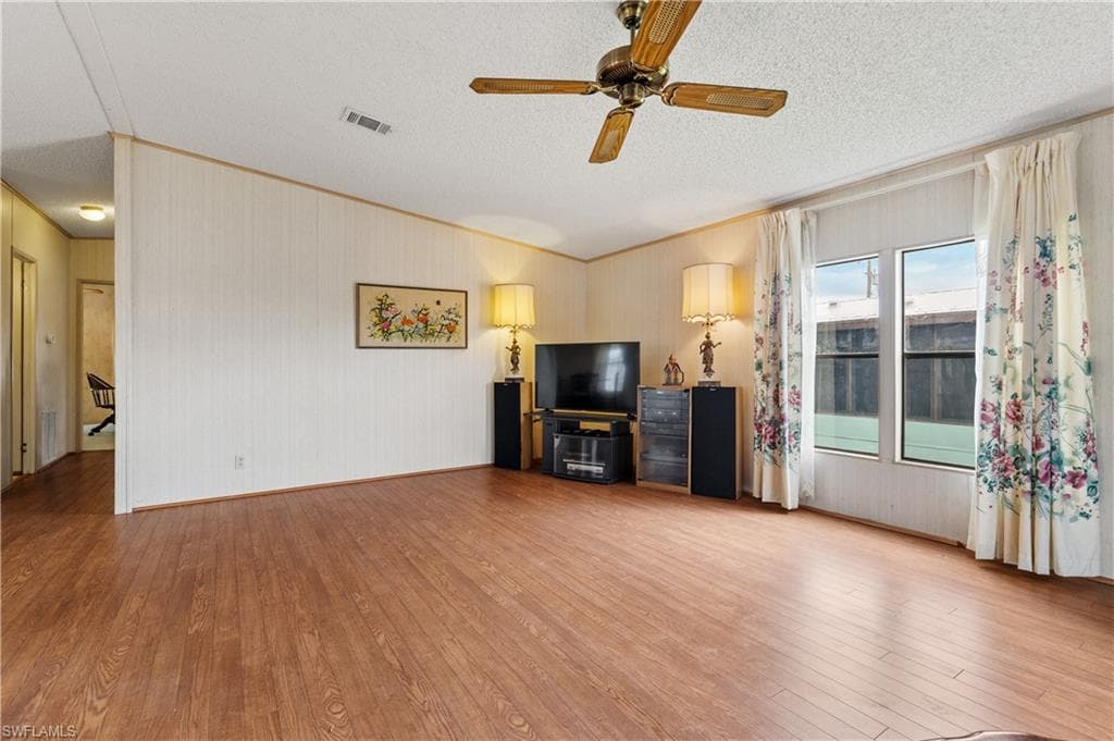 Unfurnished living room featuring ornamental molding, light wood finished floors, a ceiling fan, and a textured ceiling