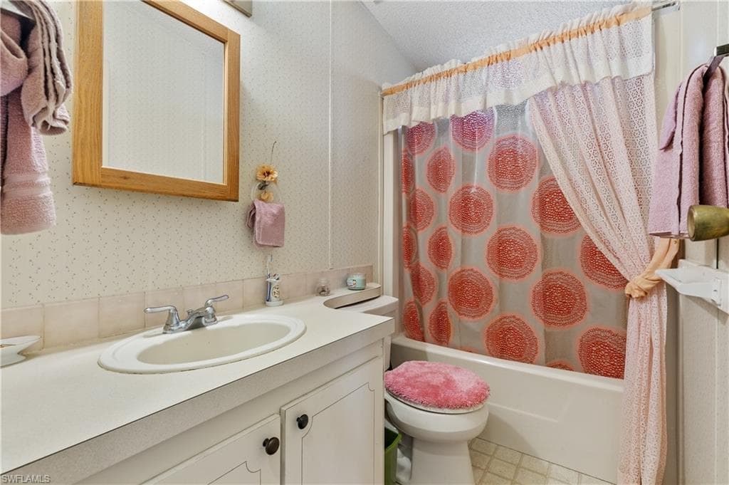 Full bathroom featuring shower / tub combo with curtain, wallpapered walls, and vanity